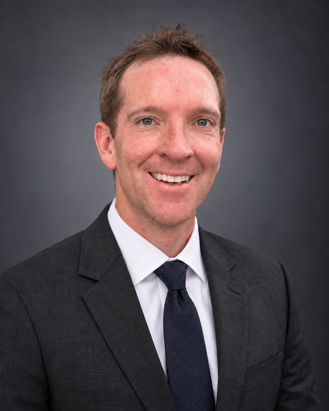 Austin Grall in a charcoal suit against a neutral studio background